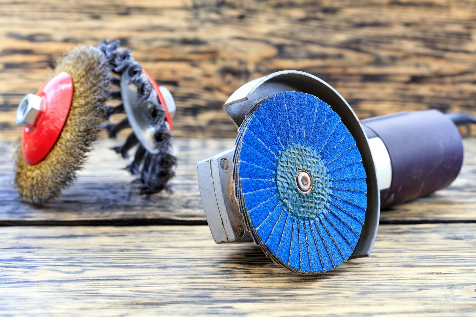 Angle grinder with grinding disc brushes and abrasive wire brushes lying on the wooden background